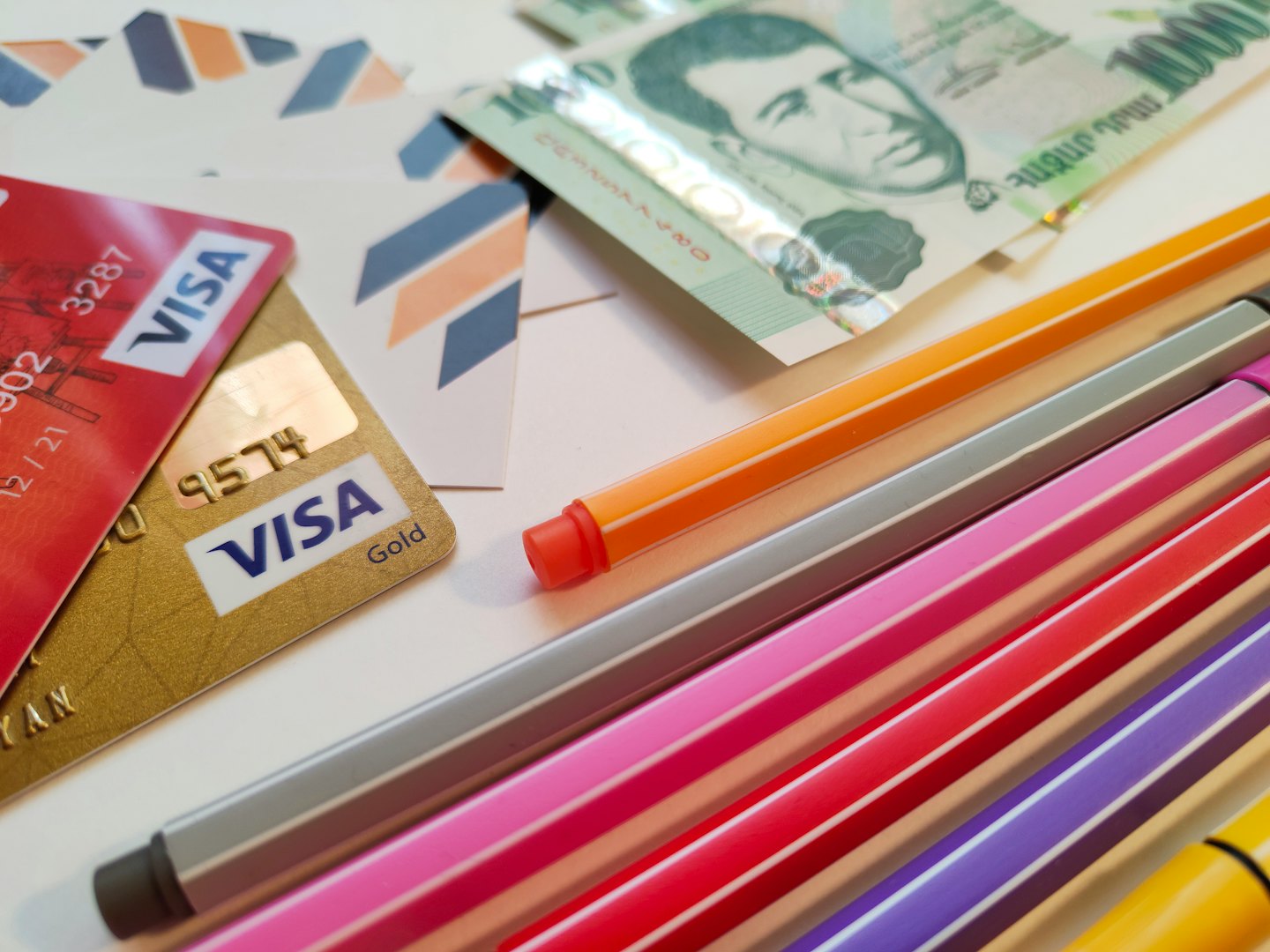 Red and gold credit cards with cash and pens.