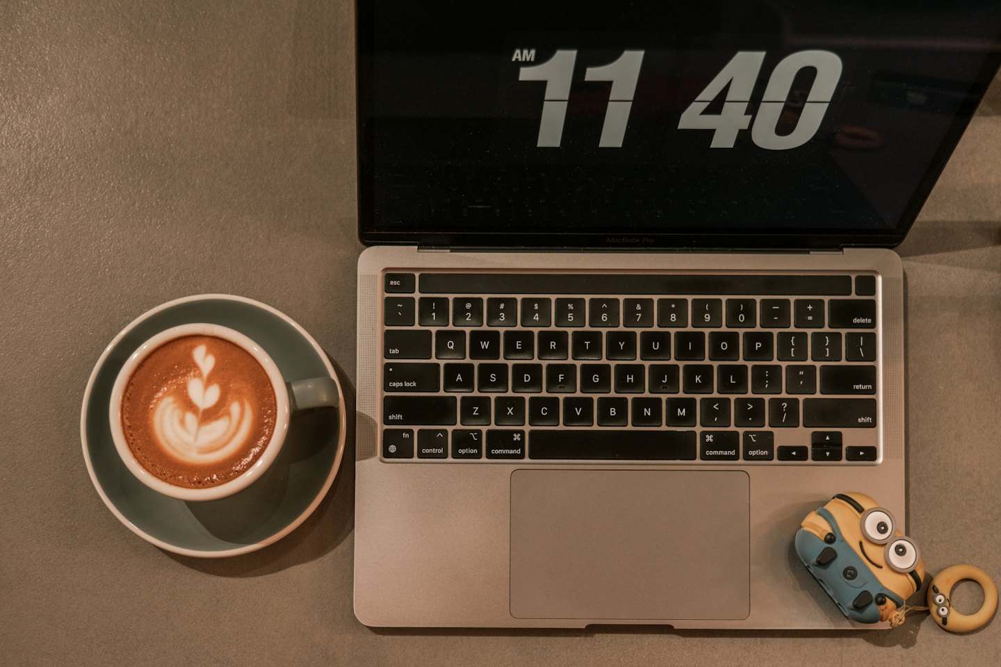 Silver laptop and teal coffee cup on a grey desk.